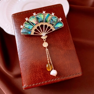 Macro view of vintage fan brooch with iridescent shell inlays and a pearl tassel