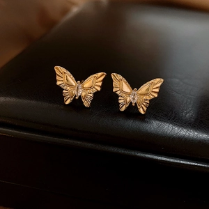 Macro view of gold butterfly stud earrings with marquise zircon on black leather