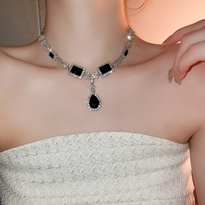 Close-up of geometric necklace featuring black gemstone and pear-shaped drop pendant