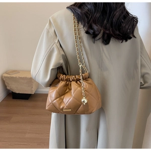 Brown quilted bucket bag with gold chain strap worn by a model in a minimalist room