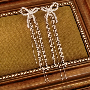 Detail view of silver bow drop earrings with white cubic zirconia on green velvet