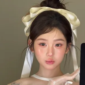 Close-up of cream satin bow hair clip with long ribbons on model with tulle gloves