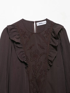 Détail de broderie florale et de volants sur un chemisier marron foncé pour femme
