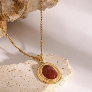 Golden stainless steel necklace with red agate pendant on natural beige stone background