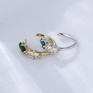 Macro shot of gold and silver ear cuffs featuring emerald green and clear square stones