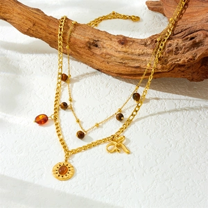 Double-layered gold necklace with sun pendant, bow charm and tiger eye beads on wood