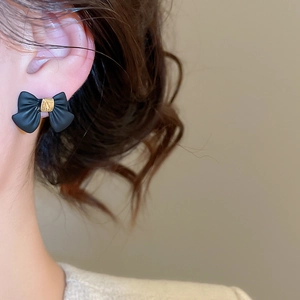 Detail view of black bow earrings with gold accents worn by a model in soft lighting