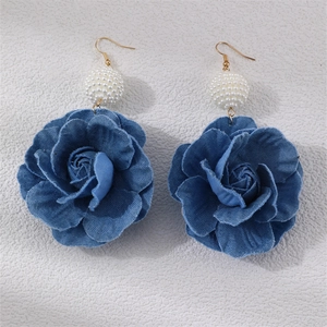 Macro detail of blue denim camellia earrings with white pearl accent and gold hooks