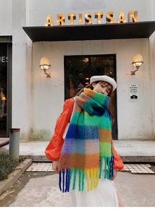 Detail of vibrant rainbow plaid knit scarf with long twisted tassels in outdoor lighting
