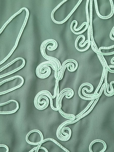 Gros plan détaillé de la broderie 3D complexe sur le tissu vert de l'ensemble dos nu
