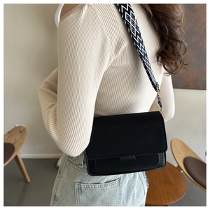 Detailed view of a black crossbody bag with a geometric pattern strap on a model