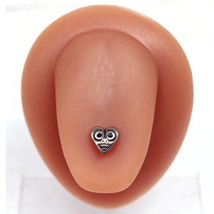 Macro view of a heart-shaped tongue ring with skull carving on a silicone tongue model