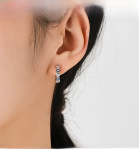 Close-up of S925 silver huggie earrings with blue evil eye and heart charms on ear