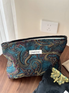 Macro detail of retro paisley jacquard makeup bag with gold embroidery and zipper