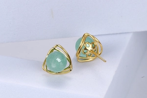 Macro view of S925 silver stud earrings with light green round stones in gold-tone frames