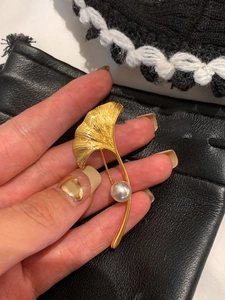 Dettaglio macro della spilla in oro 18K con texture spazzolata e perla bianca