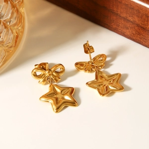 Detailed view of 18k gold plated bow and star earrings on a white surface with warm bokeh