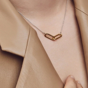 Close-up of interlocking 18K gold rectangular rings on silver chain worn on neck