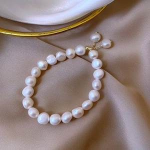 Detailed macro view of 14K gold-plated Baroque pearl bracelet on champagne silk fabric