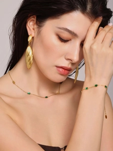 Model wearing gold jewelry set with emerald green stones and ripple hoops