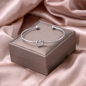 Macro view of a polished silver knot cuff bracelet resting on a silk jewelry box