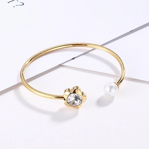 Detail of gold titanium bracelet featuring a white pearl and a crystal flower charm