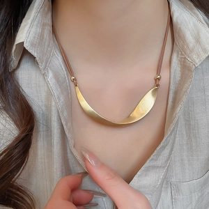 Detail of a minimalist golden matte twisted pendant necklace worn on a beige shirt