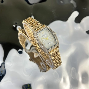 Detailed close-up of a luxury gold tonneau watch with crystal bezel on a liquid surface