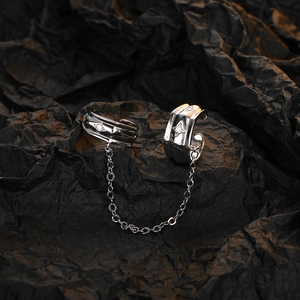 Detailed close-up of silver chain ear cuff with star patterns and zircon inlays on black background