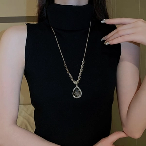 Close-up of golden teardrop crystal necklace with pavé diamonds on a black turtleneck
