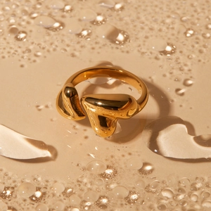 Bague cœur asymétrique plaquée or 18K avec design en métal fluide sur un fond de goutte d'eau