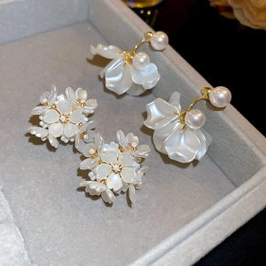 Macro shot of white floral earrings with imitation pearls on a grey velvet display tray