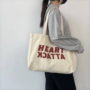Detail of a large cream canvas tote bag featuring a red Heart Attack text print design
