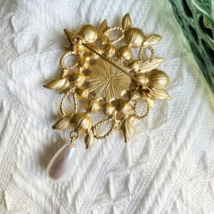 Macro detail of vintage gold brooch with cutout texture, safety pin back, and drop pearl