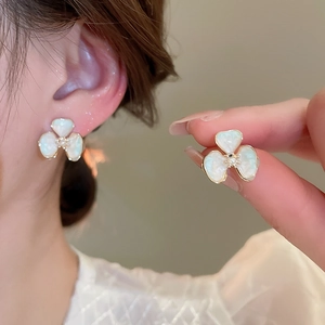 Close-up of white clover stud earring with gold border and pearl on a model ear