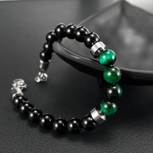 Detail of beaded men's bracelet with green tiger eye stones and black beads on dark bowl