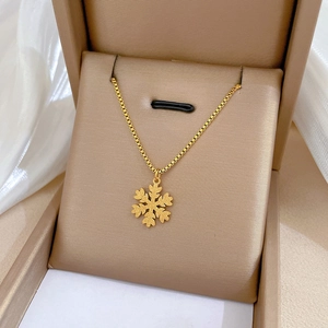 Macro view of a matte gold snowflake pendant necklace displayed in a beige jewelry gift box