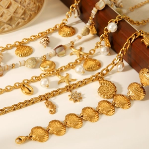 Detailed close-up of gold ocean-themed bracelet with seashell and pearl charms on wooden stand