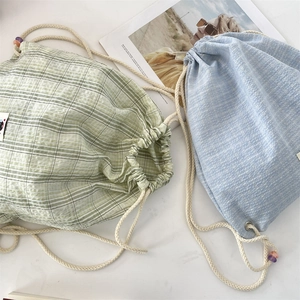 Detail of drawstring plaid canvas backpacks in green and light blue on a stone surface