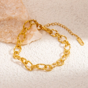 Detailed close-up of textured gold chain links and S.STEEL material tag on a beige stone surface