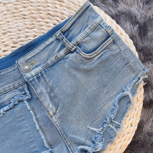 Dettaglio degli shorts in denim a vita alta con chiusura a bottone e orlo sfrangiato