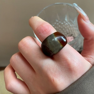 Detail view of a wide amber-colored resin ring with marble texture on finger