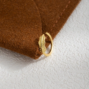 Macro detail of a gold leaf-textured ear cuff on a premium textured background