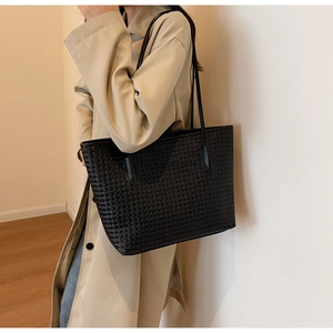 Fashionable black woven tote bag with slim shoulder straps shown on a beige trench coat