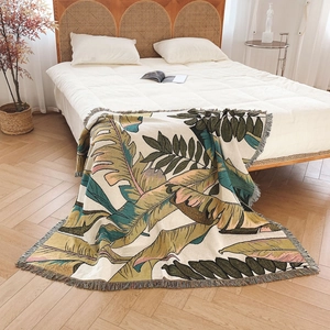 Nordic knit throw blanket with tropical leaf print and fringes on a cozy bed