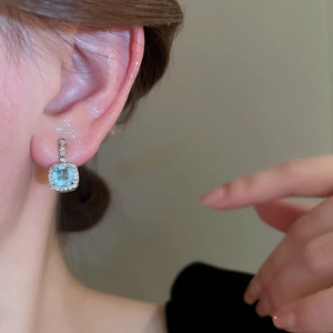 Close-up of light blue halo square stud earrings worn on a model for a refined look