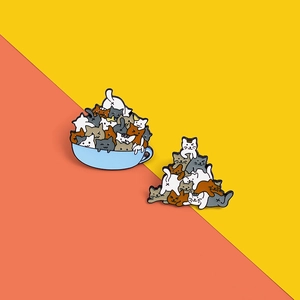 Detailed view of two enamel pins featuring stacked cats and cats in a blue teacup