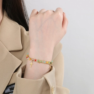 Detailed view of a gold double-layer bracelet with colorful beads and cross charms on a wrist