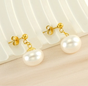Macro detail of white baroque pearl earrings with gold pins on a wavy tray