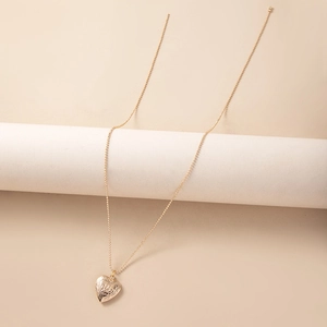 Detail of a vintage engraved gold heart locket necklace displayed on a white pedestal